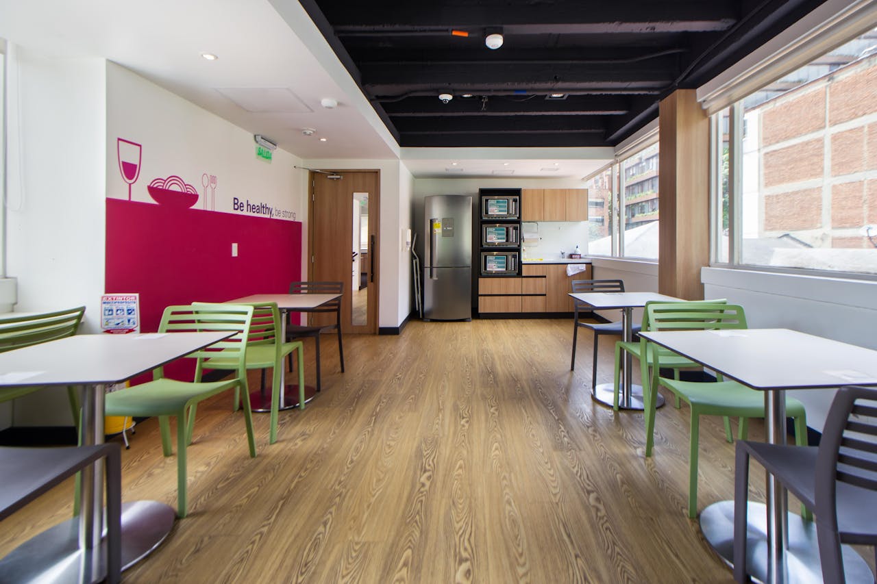 Bright and minimalist office kitchen with tables and chairs, promoting a healthy lifestyle.